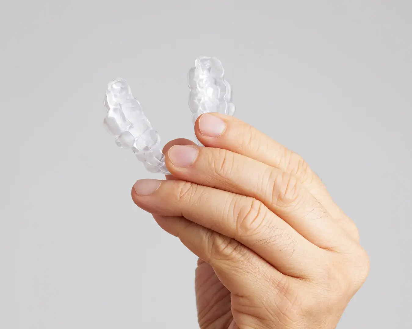 Hand holding two clear sleep apnea mouth guards against a neutral background